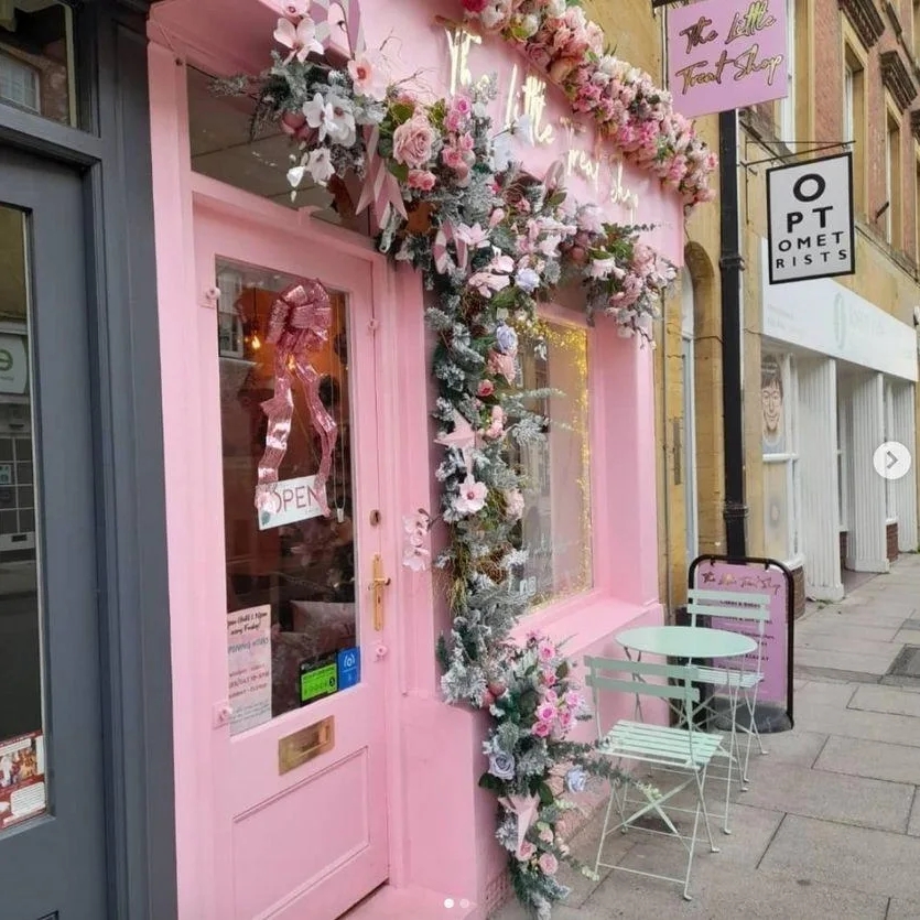 A baby pink shop front with a garland of flowers