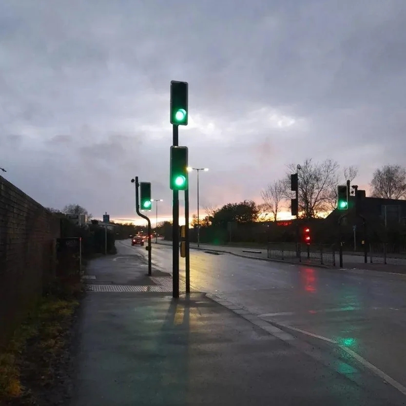 A road with a dark looming sky, low light on the horizon and traffic lights on green