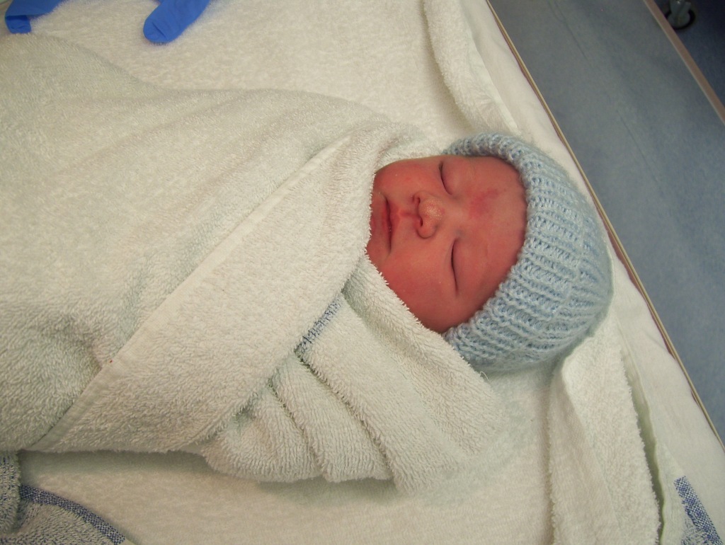 A beautiful sleeping new born baby with a knitted hat and wrapped in a towel.